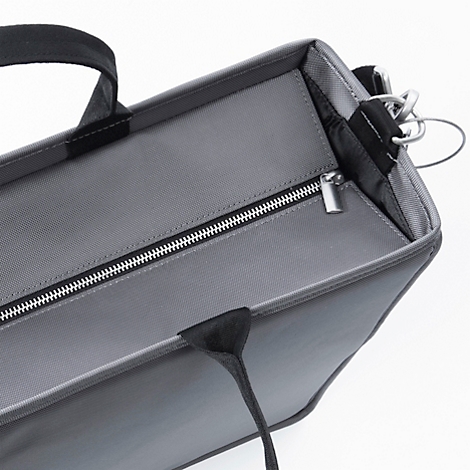 Graue Handtasche mit Reissverschluss und Henkeln. Der Fokus liegt auf den Details des Materials und des Reissverschlusses.