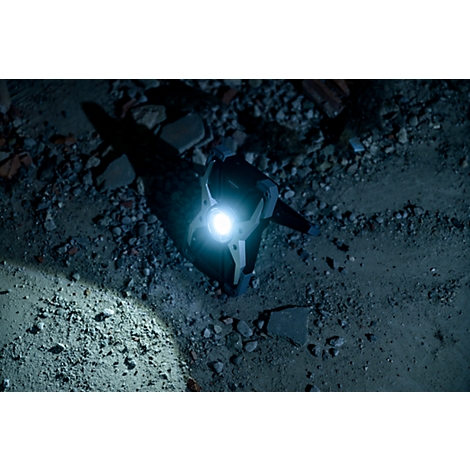 Eine Taschenlampe leuchtet auf den Boden und wirft einen Schatten auf die Steinfläche, umgeben von Schutt.
