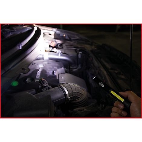 Nahaufnahme eines Motorraums, der mit einer Taschenlampe beleuchtet wird. Die Taschenlampe wird von einer Hand gehalten.