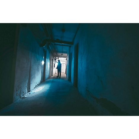Dark hallway with person at the end, bluish lighting.