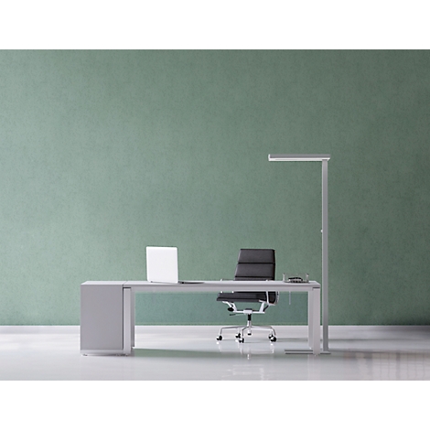 Office with desk, laptop, chair and floor lamp against a mint green wall.