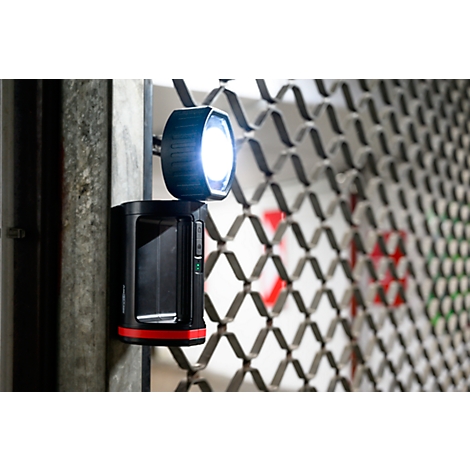 A black LED light with a red base, attached to a metal structure. The light shines brightly.