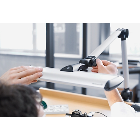Person adjusting a desk lamp. The lamp has a long, rectangular light source connected to an articulated arm.