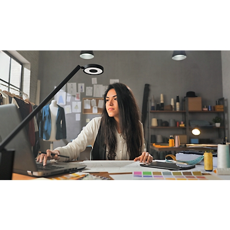 Designer working on laptop surrounded by fabric swatches, sketches, and lighting.