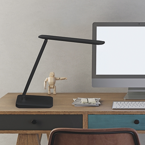 Zwarte bureaulamp op houten bureau. Daarnaast computer en houten pop.