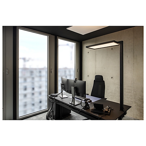 Kantoor met bureau, monitoren, bureaulamp en uitzicht door raam op gebouwen.