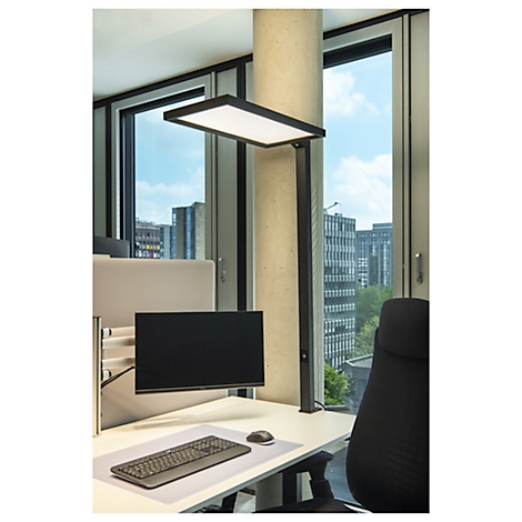 Bureau met lamp, monitor, toetsenbord en raam met uitzicht op gebouwen. Heldere verlichting, moderne kantoorinrichting.