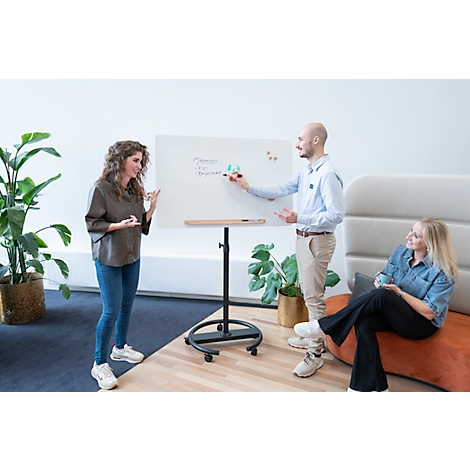 Trois personnes lors d'une présentation. Une femme montre le tableau blanc, un homme écrit, une troisième personne est assise détendue.