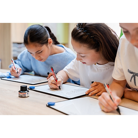 Drei Mädchen sitzen konzentriert an einem Tisch und schreiben mit Stiften auf kleine Whiteboards.