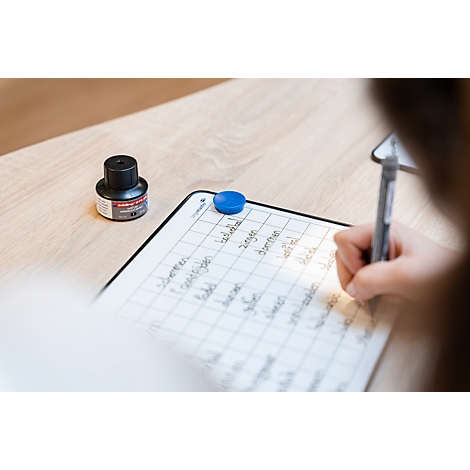 Person schreibt mit einem Stift auf einem Whiteboard mit Raster, daneben steht ein schwarzes Tintenfässchen.