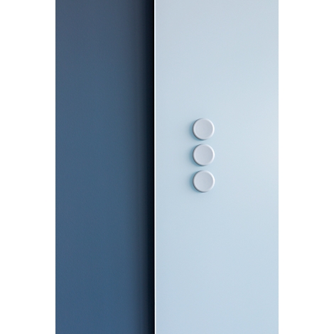 Trois interrupteurs ronds et clairs sur un mur bleu clair-blanc ; un rectangle bleu foncé à gauche.