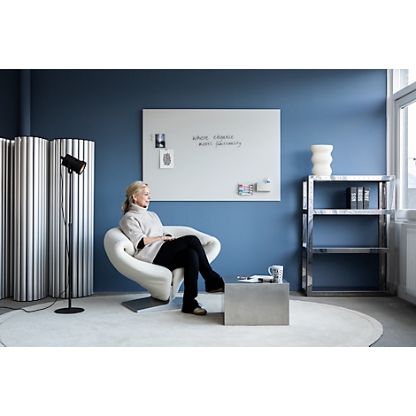 Une femme est assise dans un fauteuil blanc dans une pièce bleue. Un tableau blanc affiche "Where ideas meet ingenuity".
