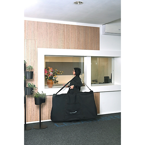 Person in black carrying a large black bag over their shoulder. Background: windows, flowers, plants.