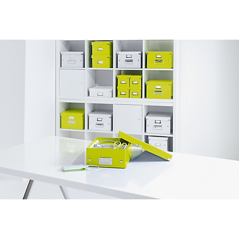 An open lime green box with cables and paper in front of a white shelf full of boxes.