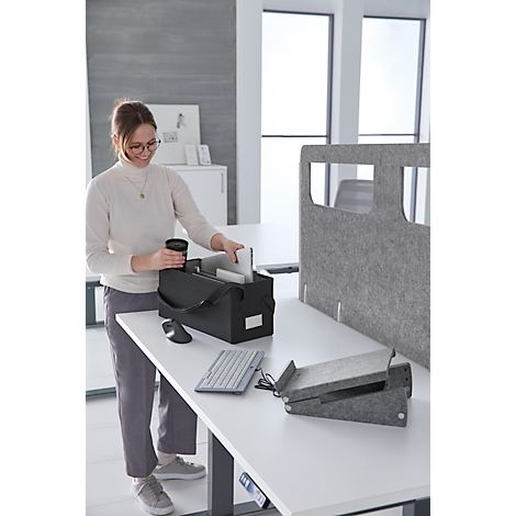 Frau am Schreibtisch mit schwarzer Tasche. Sie legt Gegenstände hinein. Auf dem Tisch liegen Maus, Tastatur und graue Unterlagen.