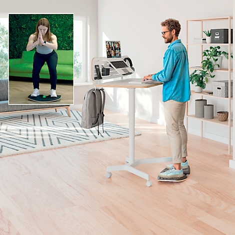 Een man staat aan een zit-sta bureau, een vrouw traint op een balansbord. Op de achtergrond een woonkamer.