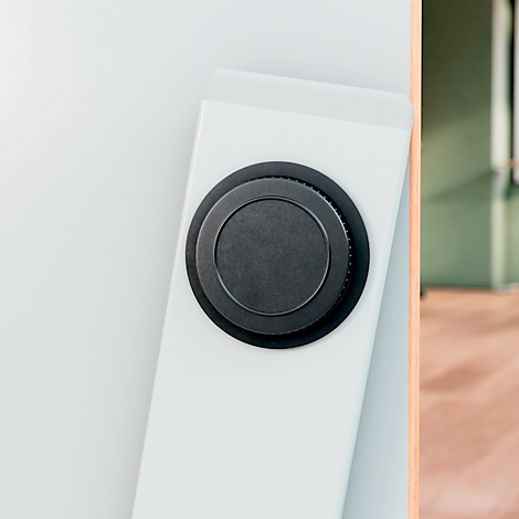 Black knob set in a white frame. The background is blurred, showing wood and a green wall.