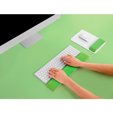 Person typing on keyboard with wrist rest. Mouse and monitor on green surface.