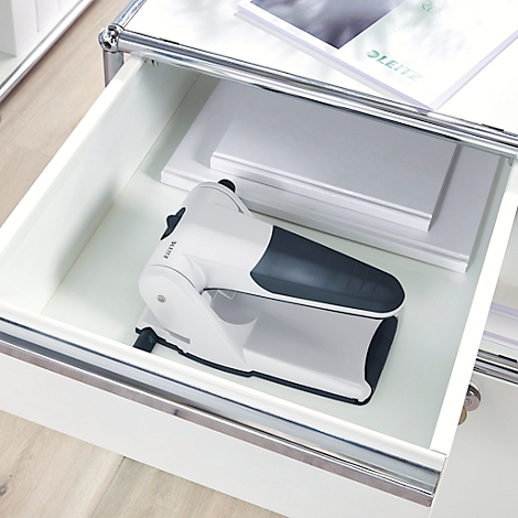 A white hole punch with a dark tip in a drawer. Papers and brochure next to it.