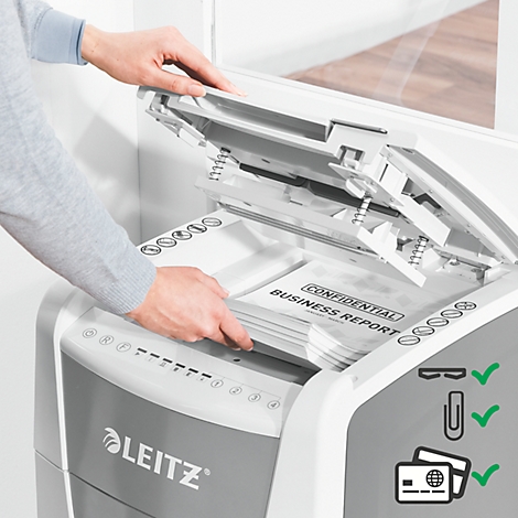 Person placing documents into a paper shredder. The documents say "Confidential Business Report". The device displays the Leitz logo.