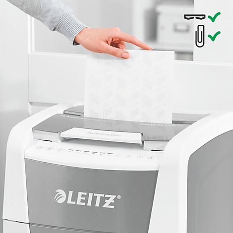 A hand places paper into a shredder. There is a pattern on the paper.