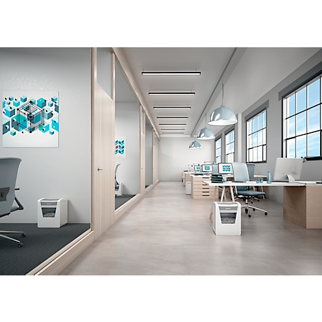 Een kantoorruimte met bureaus, computers, een prullenbak en ramen. Een papierversnipperaar staat op de voorgrond.