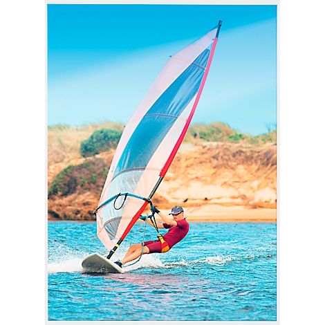 Windsurfer on the water, the sail is white with blue and red accents. The sky is blue.