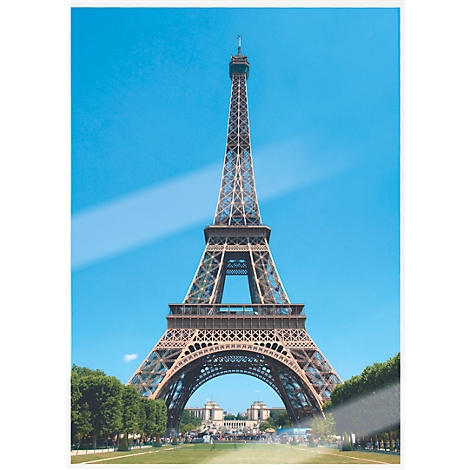 Eiffel Tower in Paris. Blue sky, green trees at the base.