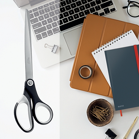 Große Schere auf einem weißen Schreibtisch, daneben ein Laptop, Notizbücher und Büroaccessoires.
