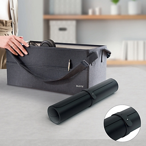 Eine Person öffnet eine graue Stofftasche mit Henkeln. Daneben liegt eine aufgerollte schwarze Schreibtischunterlage.