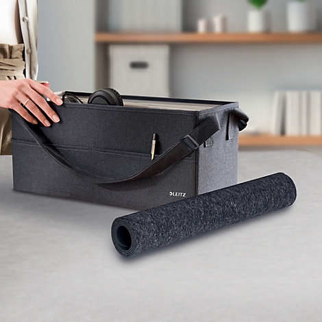 Boîte de rangement gris foncé avec contenu et tapis enroulé.