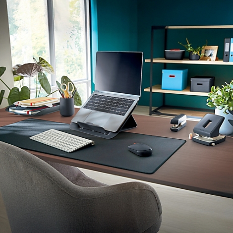 Bureau avec ordinateur portable, souris, clavier et perforatrice ; fenêtre et étagère en arrière-plan.