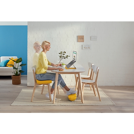 Vrouw die aan tafel op een laptop werkt. Ze gebruikt een geel voetensteunkussen.