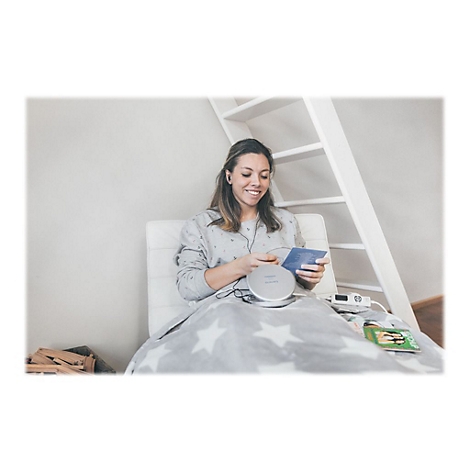 LÃ¤chelnde Frau hÃ¶rt mit KopfhÃ¶rern Musik vom CD-Player im Bett. Decke mit Sternenmuster.