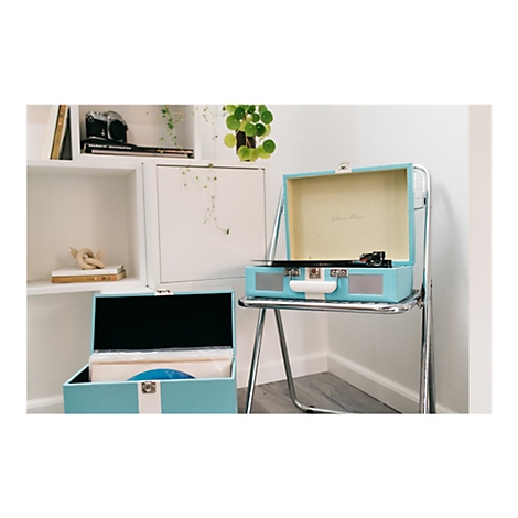 Ein hellblaues Retro-Plattenspieler-Set, das offen auf einem Stuhl steht, eine weitere Box steht daneben. Im Hintergrund ein Regal mit Dekoration.