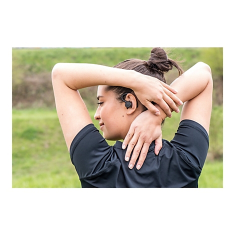 Eine Frau mit Dutt-Frisur, die sich im Freien dehnt. Sie trÃ¤gt einen schwarzen OhrhÃ¶rer.