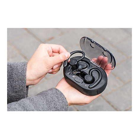 Person hÃ¤lt schwarze kabellose KopfhÃ¶rer in Ladebox. Transparentes Cover, OhrenhÃ¶rer mit BÃ¼gel.