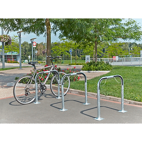 Fiets geparkeerd in fietsenrekken op asfalt, bomen en groene zones op de achtergrond.