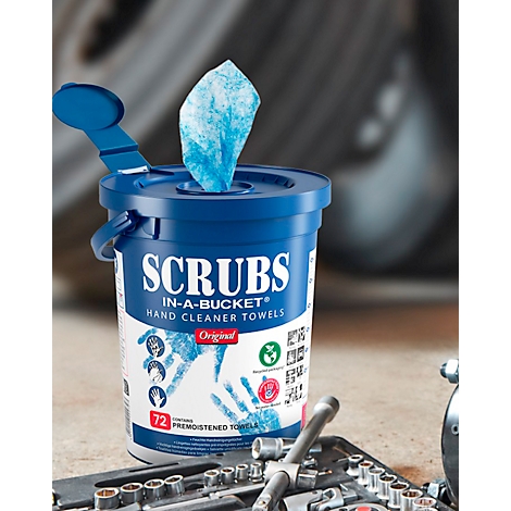 Boîte de lingettes bleues avec l'inscription "SCRUBS". Une lingette dépasse. Outils au premier plan.