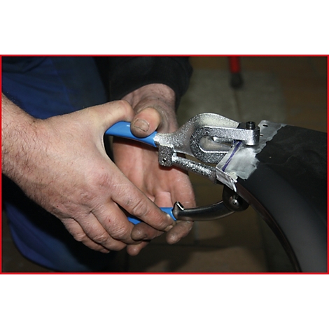 Eine Person benutzt eine Zange mit blauen Griffen, um an einem schwarzen Objekt zu arbeiten.