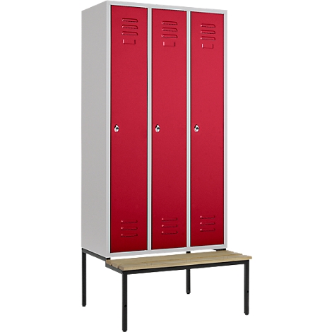 Red lockers with ventilation slots and a white cabinet stand on a bench with a black metal frame.