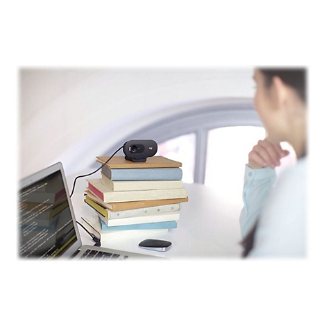 Webcam auf BÃ¼chern vor Laptop. Person im Hintergrund.