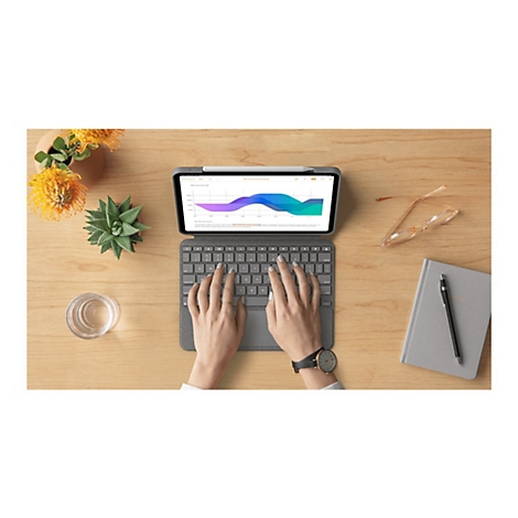 Person tippt auf Tablet-Tastatur, Diagramm-Anzeige. Holz-Arbeitsplatte mit Schreibwaren, Uhr, Glas, Pflanze.