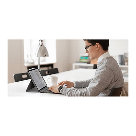 Ein Mann in Brille tippt auf einer Tastatur. Ein Tablet mit Display ist in der Nähe. Auf dem Tisch steht eine Tasse.