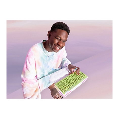 Ein Mann mit Regenbogen-Sweatshirt hält grüne Tastatur; er lächelt und zwinkert. Hintergrund ist zweifarbig.