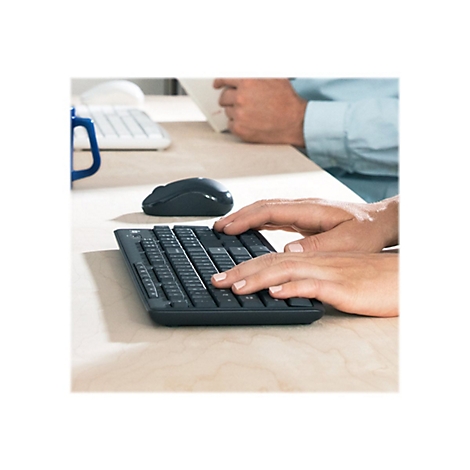 Nahaufnahme einer Person, die auf einer schwarzen, kompakten Tastatur tippt. Auf einem hellen Holztisch liegen auch eine Maus und ein Teil eines anderen Arbeitsplatzes.