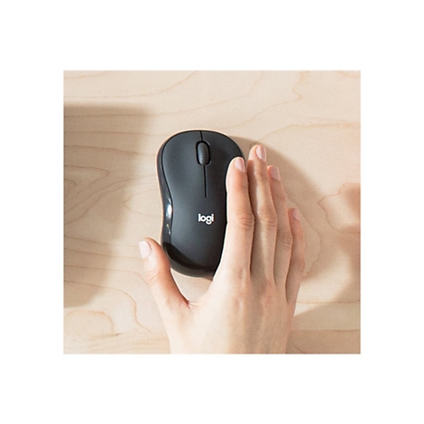 Schwarze Logitech-Maus auf hellem Holz. Eine Hand berührt die Maus.