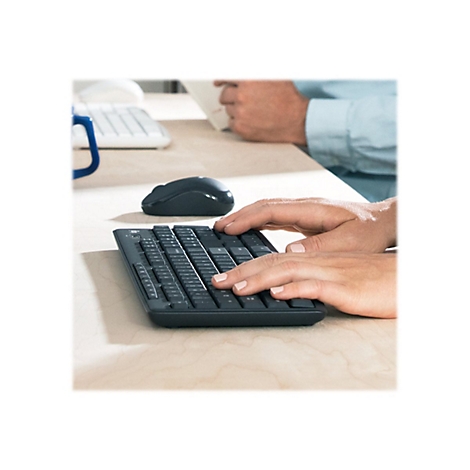 Person tippt auf einer schwarzen Tastatur. Im Hintergrund ein anderer Mensch und ein Maus.