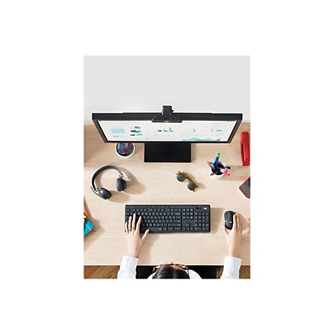 Nahaufnahme einer Person an einem Schreibtisch mit Tastatur, Maus, Monitor und Zubehör. Die Person benutzt die Tastatur.