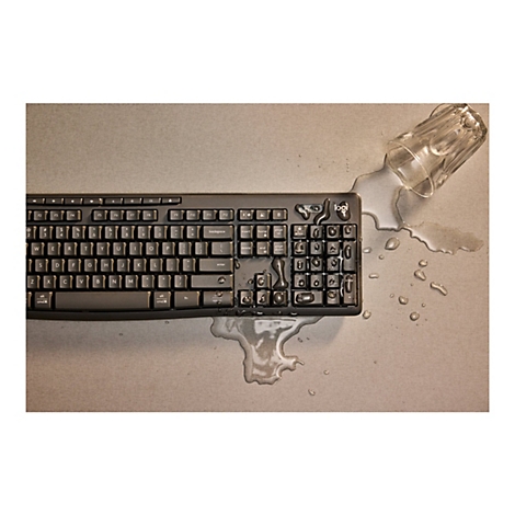 Ein schwarzes Logitech-Keyboard liegt auf einem beigen Untergrund, bedeckt von ausgelaufenem Wasser und einem umgekippten Glas.
